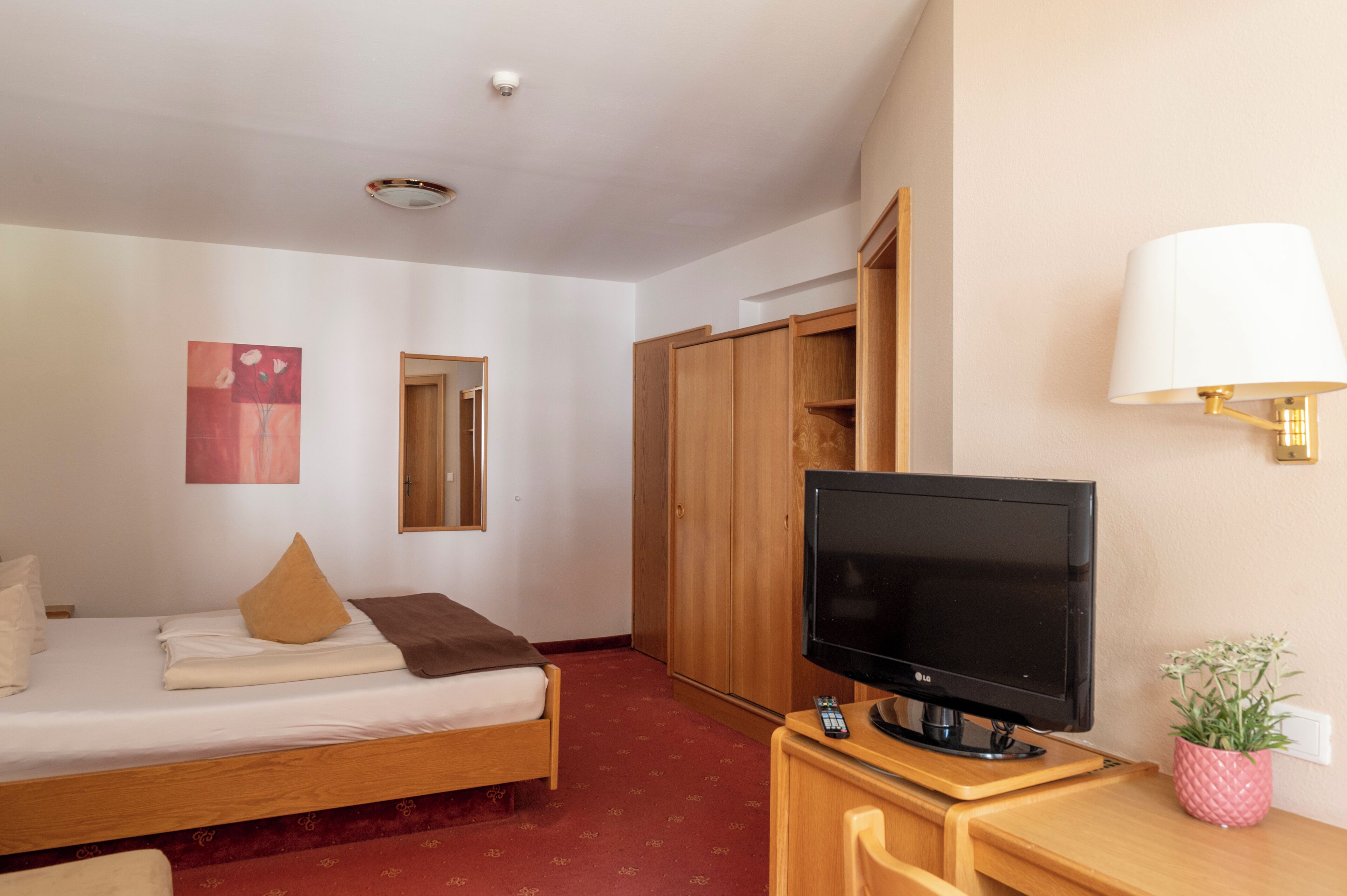 Hotellihuone, jossa on sänky, televisio, työpöytä lampun kanssa ja vaatekaappi.