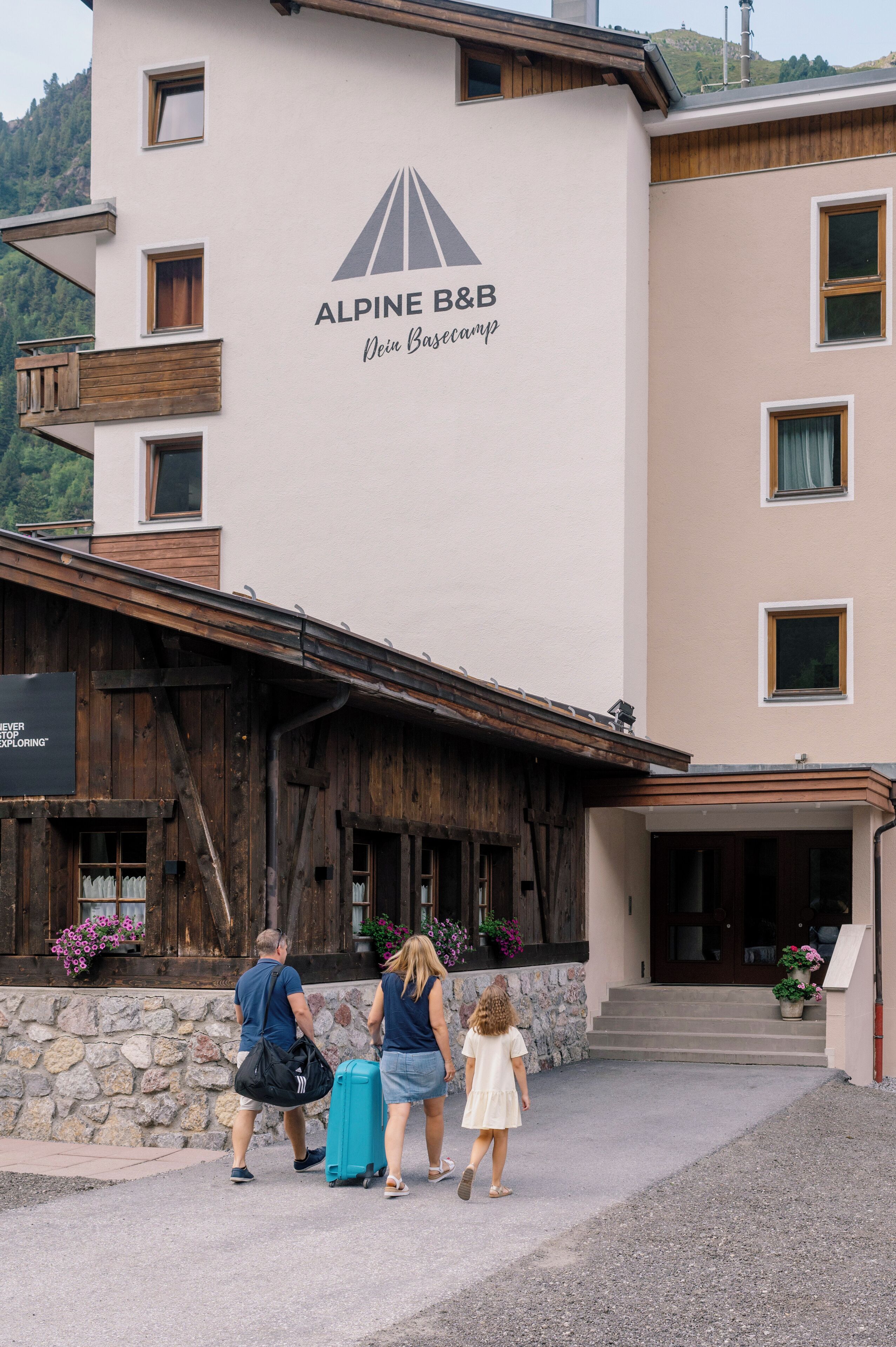Un edificio con un letrero que dice 'ALPINE B&B Dein Basecamp' y fachada de madera.