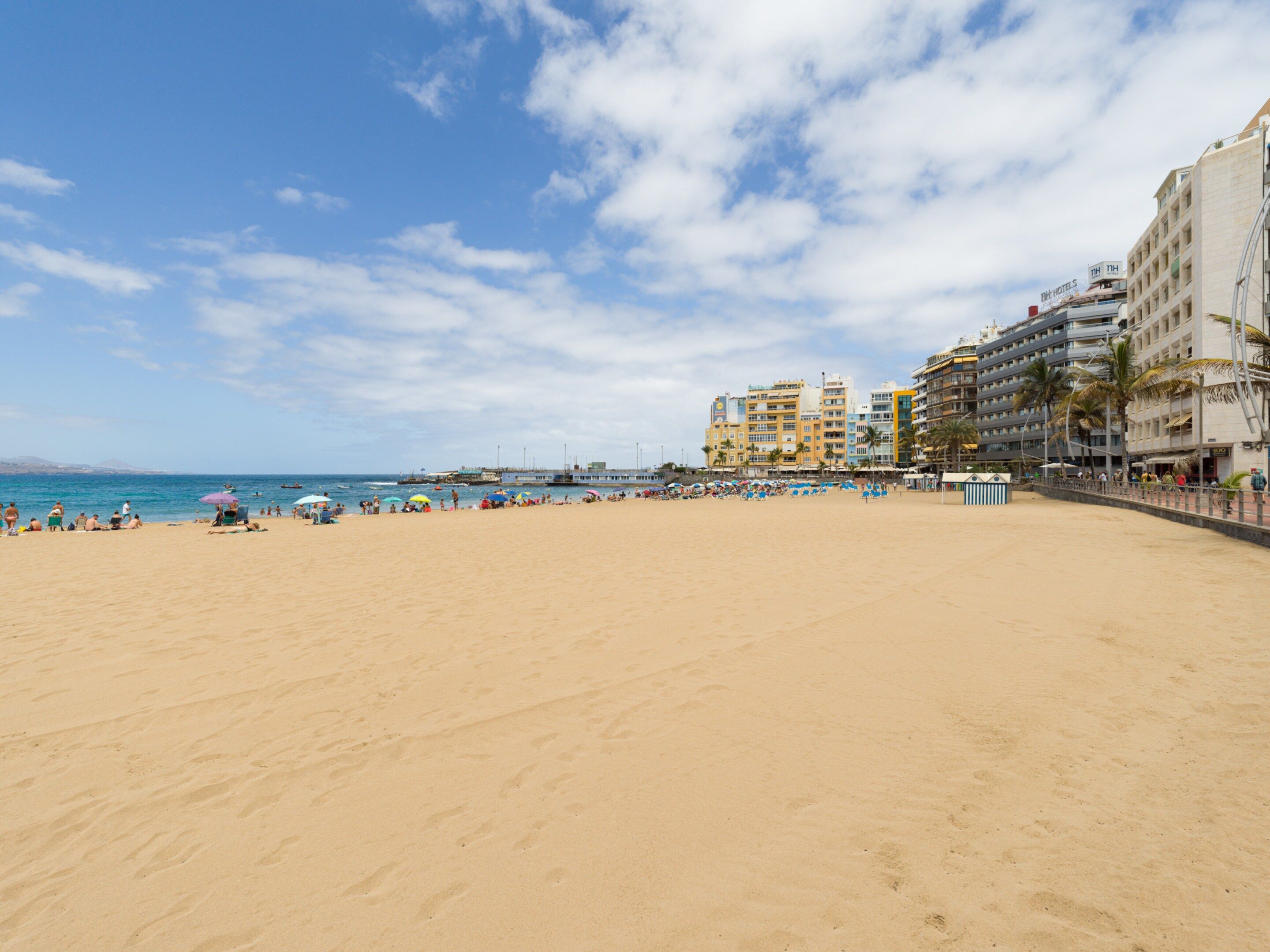 Uma praia com areal, um cais e edifícios ao fundo.