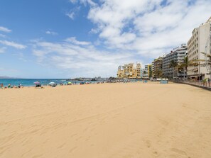 Una playa con arena, un muelle y edificios al fondo.