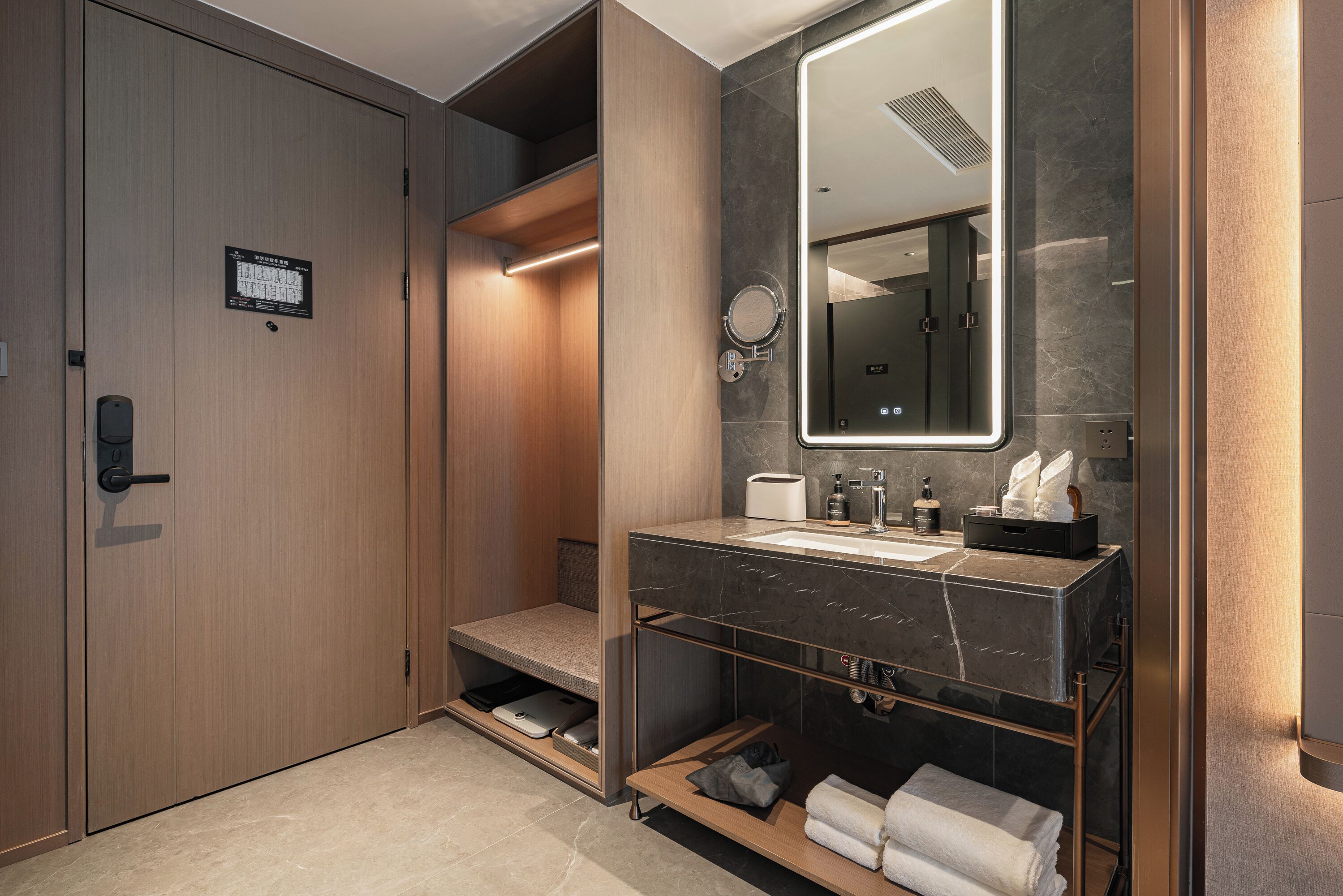 A modern bathroom with a wooden door, a marble sink, and a built-in mirror.