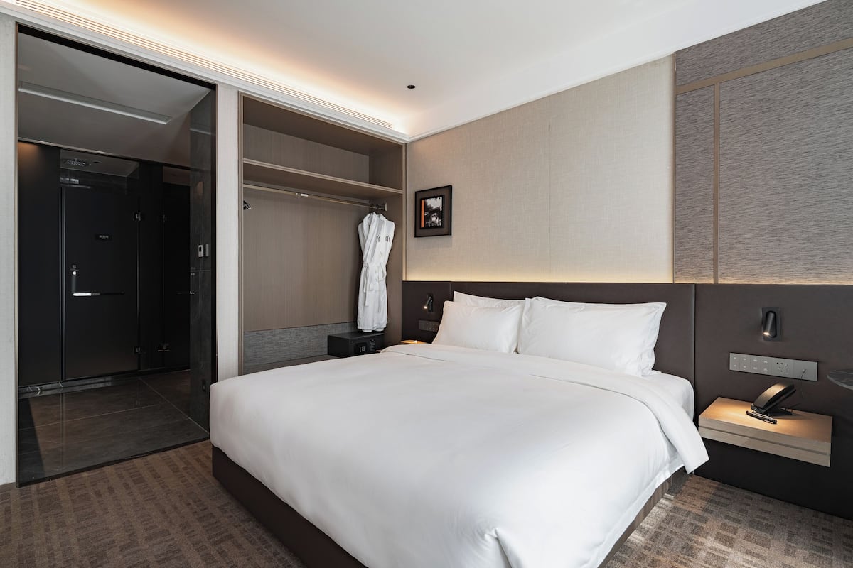 Ein modernes Hotelzimmer mit einem großen Bett, einem begehbaren Kleiderschrank und einem Badezimmer mit Glastür.