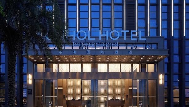 Una entrada de hotel moderna con fachada de vidrio, señalización iluminada y un área de acceso cubierta.