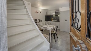 A modern kitchen with white cabinets, a dining table with chairs, and a staircase leading to another level. - Welcome to Les Volets Azur, a lovely fully renovated village house, ideal for a romantic getaway in the heart of Menthon-Saint-Bernard. Nestled between lake and mountains, this cozy home offers a peaceful and warm atmosphere. (Menthon-Saint-Bernard)