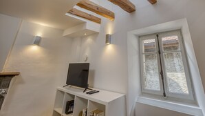 A modern room with exposed wooden beams, a white wall, a built-in TV shelf, and a window with a view of the outside. - Welcome to Les Volets Azur, a lovely fully renovated village house, ideal for a romantic getaway in the heart of Menthon-Saint-Bernard. Nestled between lake and mountains, this cozy home offers a peaceful and warm atmosphere. (Menthon-Saint-Bernard)