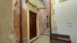 A narrow alleyway with a wooden door, a bench, and a trash bin.