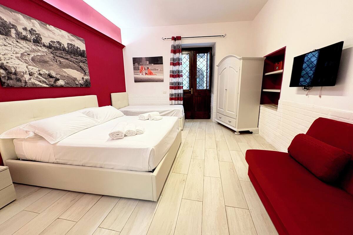 A bedroom with a bed, a red sofa, a TV, and a wardrobe.