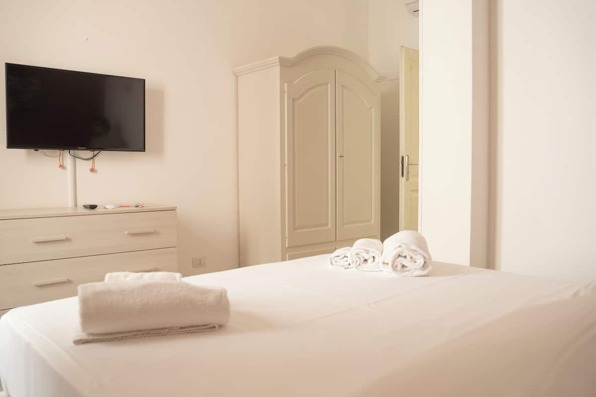 A hotel room with a bed, a TV mounted on the wall, a wardrobe, and a door leading to another room.
