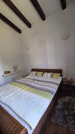 Una camera da letto con un letto, un comodino, una lampada, uno specchio e una mensola con cesti.