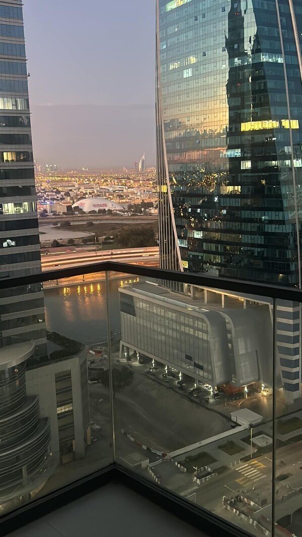 A high-rise building with a modern glass facade, a view of a cityscape with illuminated buildings, and a bridge in the distance.