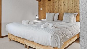 A bed with white linens, wooden headboard, and a small bedside lamp. - Piscine, Ski & Vue sur le lac – Crans 6 pers (Crans-Montana)