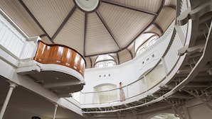 Un interior de varios niveles con cúpula central, barandillas blancas y una escalera.