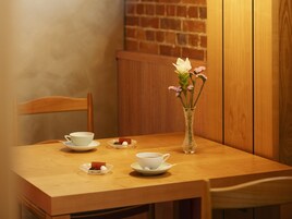 A wooden table with a vase of flowers, two cups, and a plate with food.