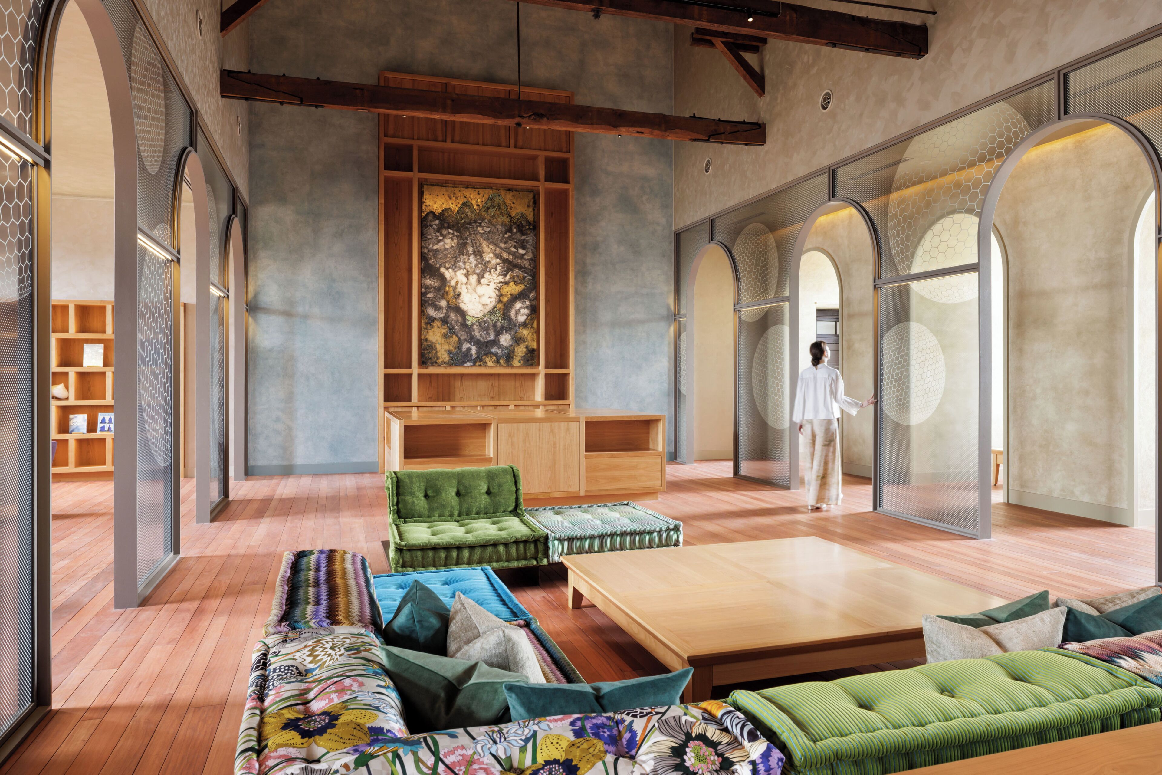 A spacious living area with a large sofa, a coffee table, and a green armchair. There is a wooden cabinet and a large artwork on the wall.