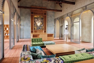 Un amplio salón con un sofá grande, una mesa de centro y un sillón verde. Se observa un mueble de madera y una obra de arte de gran tamaño en la pared.
