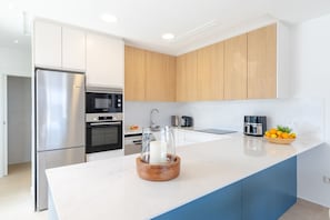 Una cocina moderna con refrigerador de acero inoxidable, horno empotrado, microondas y cafetera.