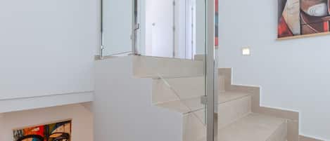 A staircase with glass railings and beige steps, leading to a room with a white door.