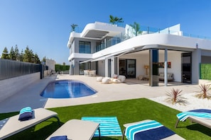 Una casa moderna de dos pisos con piscina, mobiliario exterior y un patio cubierto.