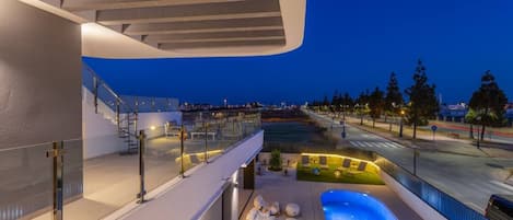A modern building with a rooftop pool, outdoor seating, and a view of the cityscape at dusk.