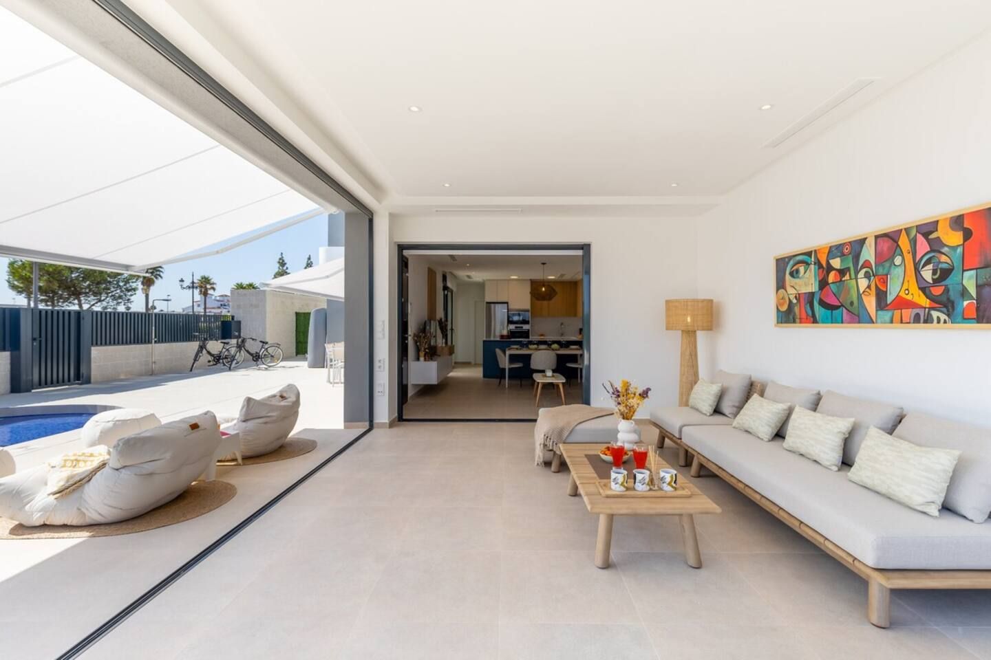 A modern living room with a sofa, coffee table, and a pool area visible through an open door.