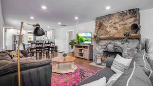 A modern living room with a stone fireplace, a dining area, and a kitchen visible through an open door. - Spacious Modern | Groups |Family |Sloans lake (Denver)