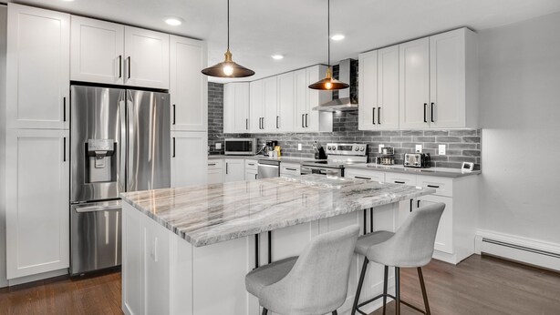 A modern kitchen with white cabinets, stainless steel appliances, a marble island, and bar stools. - Spacious Modern | Groups |Family |Sloans lake (Denver)