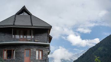 A stone building with a balcony, a peaked roof, and a mountain backdrop.
