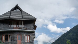 A stone building with a balcony, a peaked roof, and a mountain backdrop. - Zostel Homes Rajgundha (Multhan)