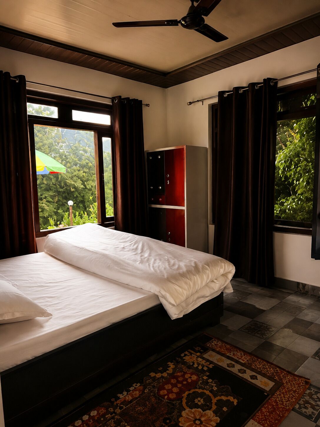A bedroom with a bed, a wardrobe, a ceiling fan, and large windows with curtains.