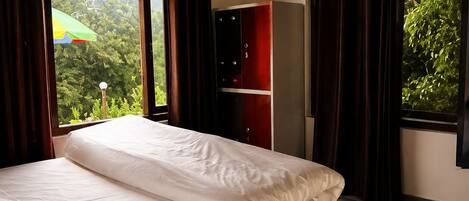 A bedroom with a bed, a wardrobe, a ceiling fan, and large windows with curtains.