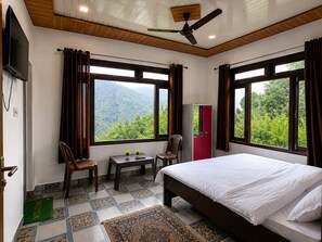 A hotel room with a bed, two chairs, a small table, a TV, and a wardrobe. - Cozy Mukteshwar homestay with Himalayan views and warm local hospitality. (nainital)