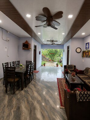 A room with a dining table and chairs, a sofa, a ceiling fan, and a view of a garden. - Cozy Mukteshwar homestay with Himalayan views and warm local hospitality. (nainital)