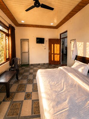 A bedroom with a bed, a desk, a chair, a television, and a ceiling fan. - Cozy Mukteshwar homestay with Himalayan views and warm local hospitality. (nainital)