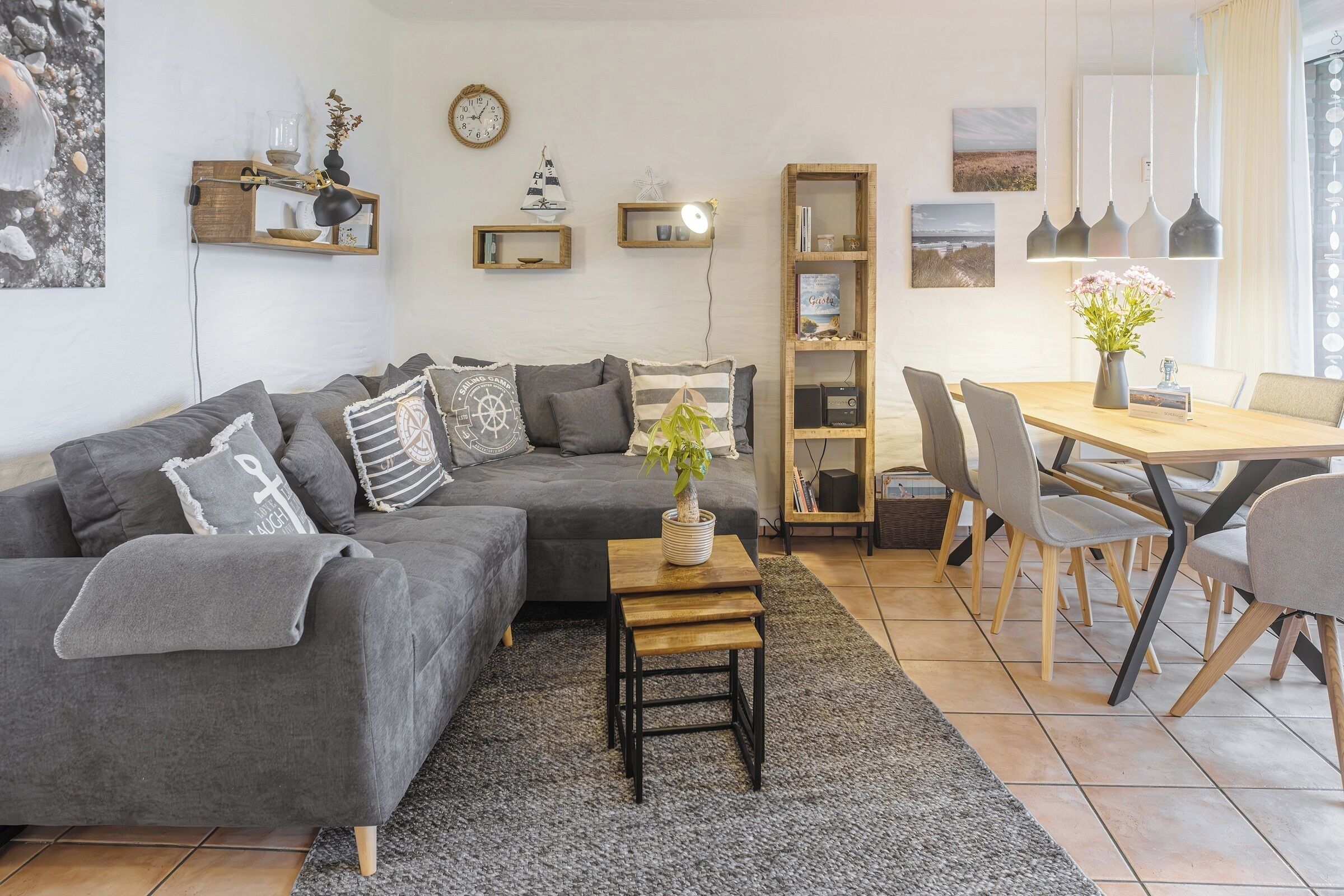 A modern living room with a grey sectional sofa, a wooden coffee table, and a dining area with a wooden table and chairs.