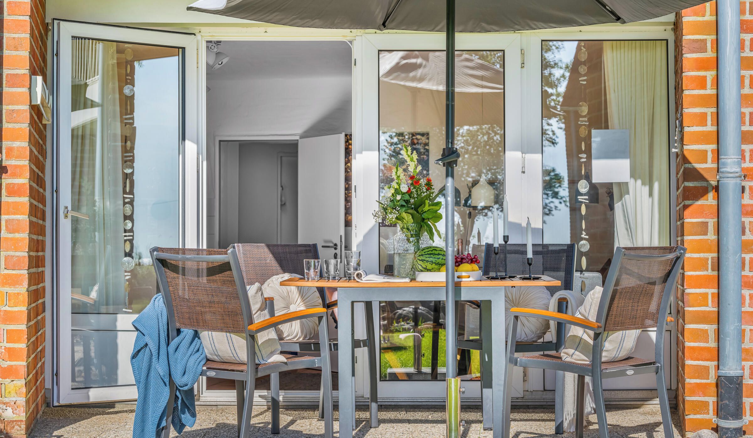 Un patio con una mesa, sillas, una puerta de vidrio que da a una habitación y una lámpara colgante.