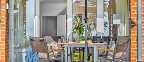 Un patio con una mesa, sillas, una puerta de vidrio que da a una habitación y una lámpara colgante.