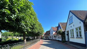 A cobblestone street lined with traditional European-style buildings, a metal fence, and lush green trees.