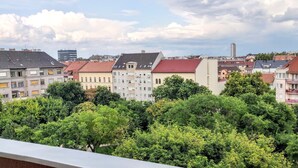 A cityscape with various buildings, including residential and commercial structures, and dense greenery in the foreground.
