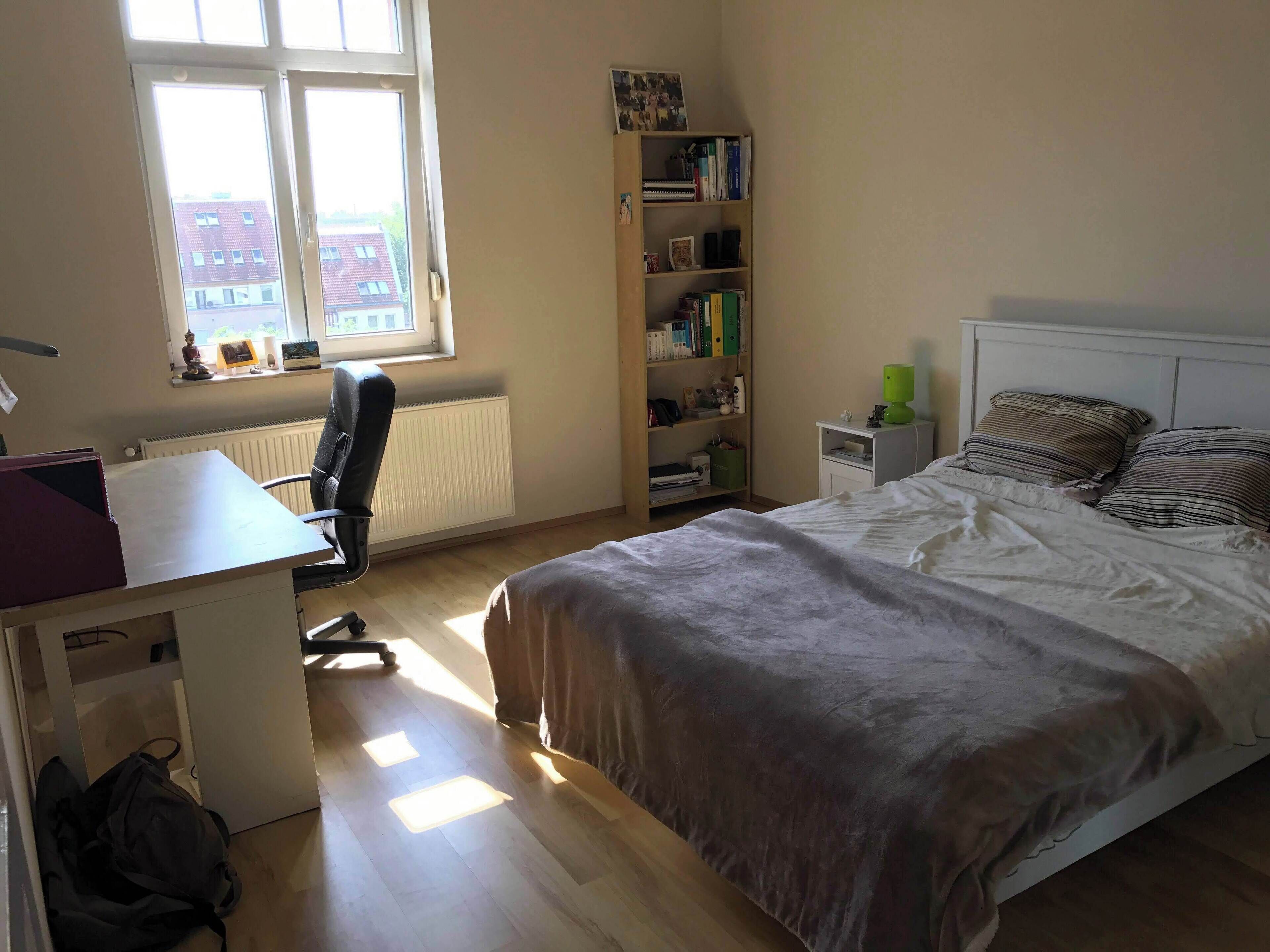 Ein Schlafzimmer mit einem Bett, einem Schreibtisch, einem Stuhl, einem Bücherregal und einer Heizung.