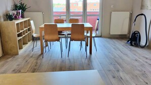 A dining area with a table and chairs, a radiator, a vacuum cleaner, and a view of buildings outside.