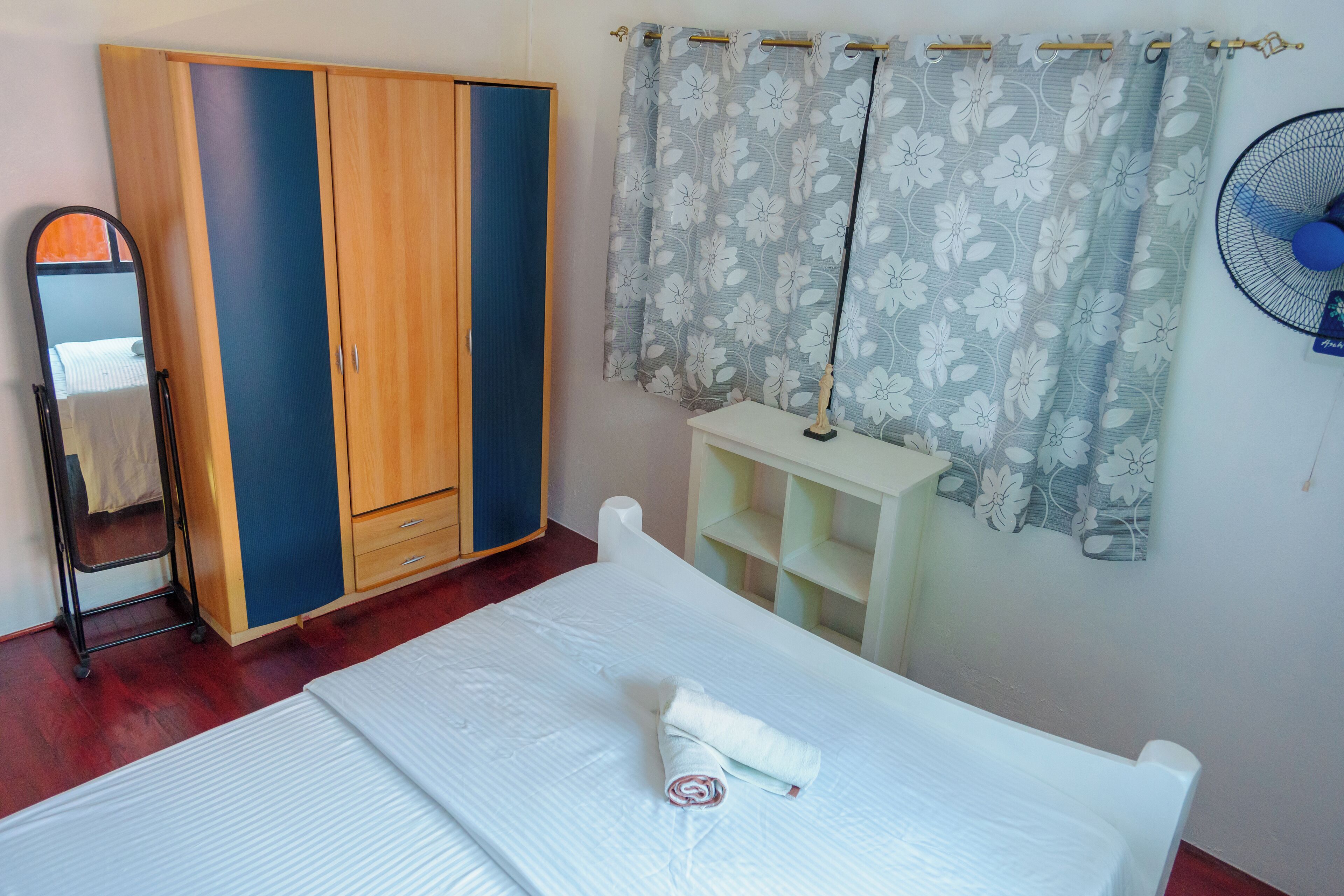 Un dormitorio con cama, armario, espejo, ventilador y cortina.