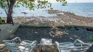 A beachside seating area with metal chairs and a small table, overlooking a rocky shoreline with boats in the water. - Silang Beach Resort and Diving (Dauin)