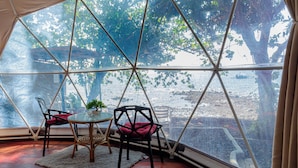 A tented room with a table and chairs, a small plant, and a view of a body of water and trees. - Silang Beach Resort and Diving (Dauin)