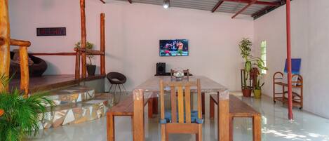 Uma sala de jantar com uma grande mesa de madeira e cadeiras, uma televisão na parede e um letreiro de varanda.