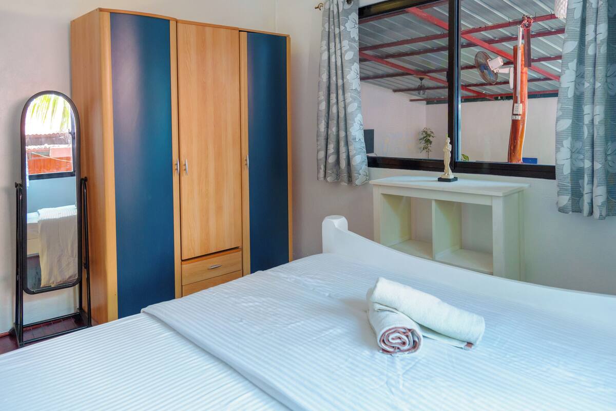 Une chambre d’hôtel avec un lit, une armoire, un miroir et une fenêtre avec des rideaux.