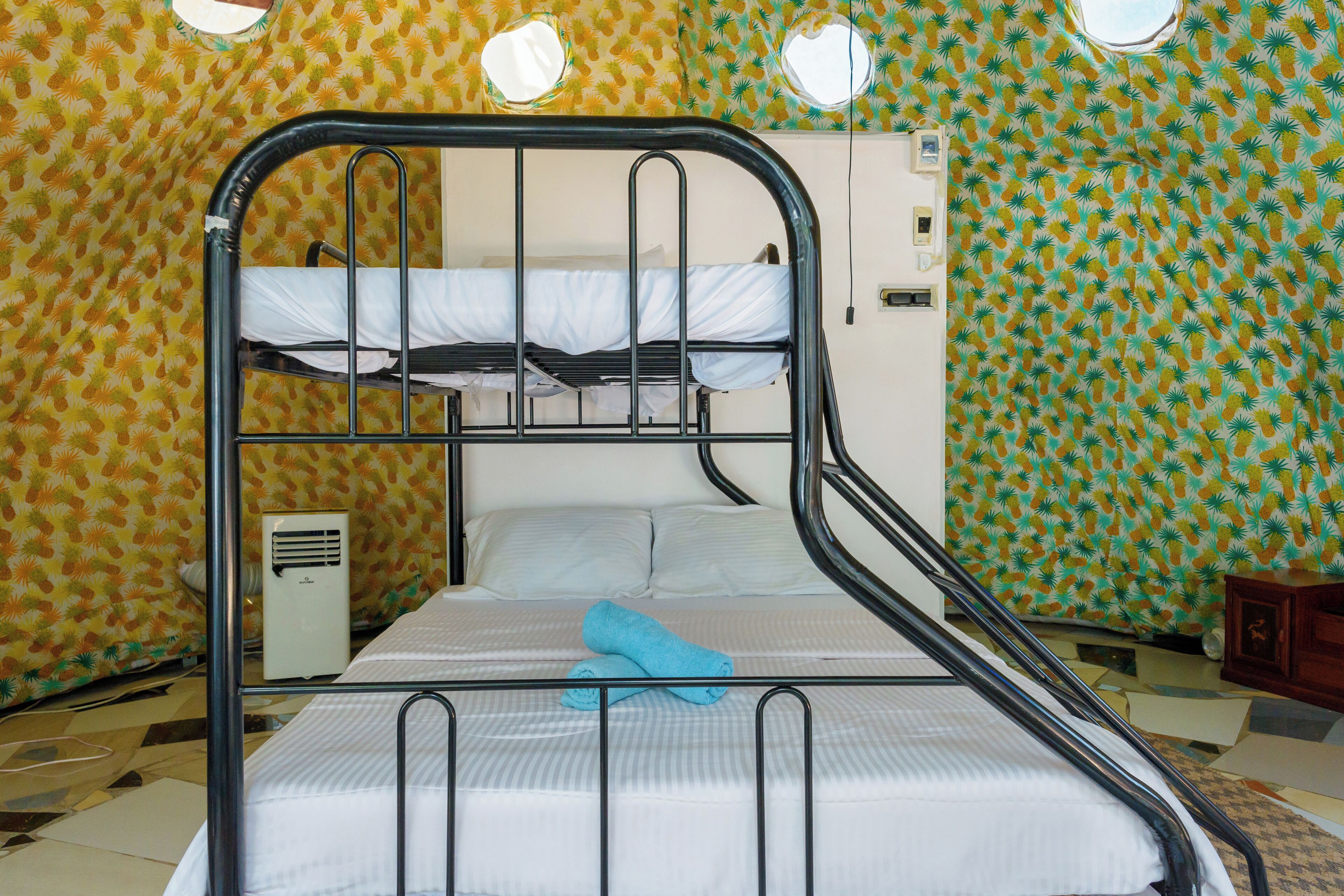 A bunk bed with a white mattress and a blue towel, a white heater, and a patterned wall.