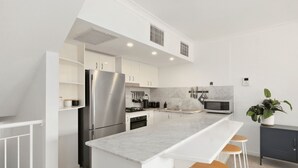 A modern kitchen with white cabinetry, stainless steel appliances, a marble countertop, and bar stools.