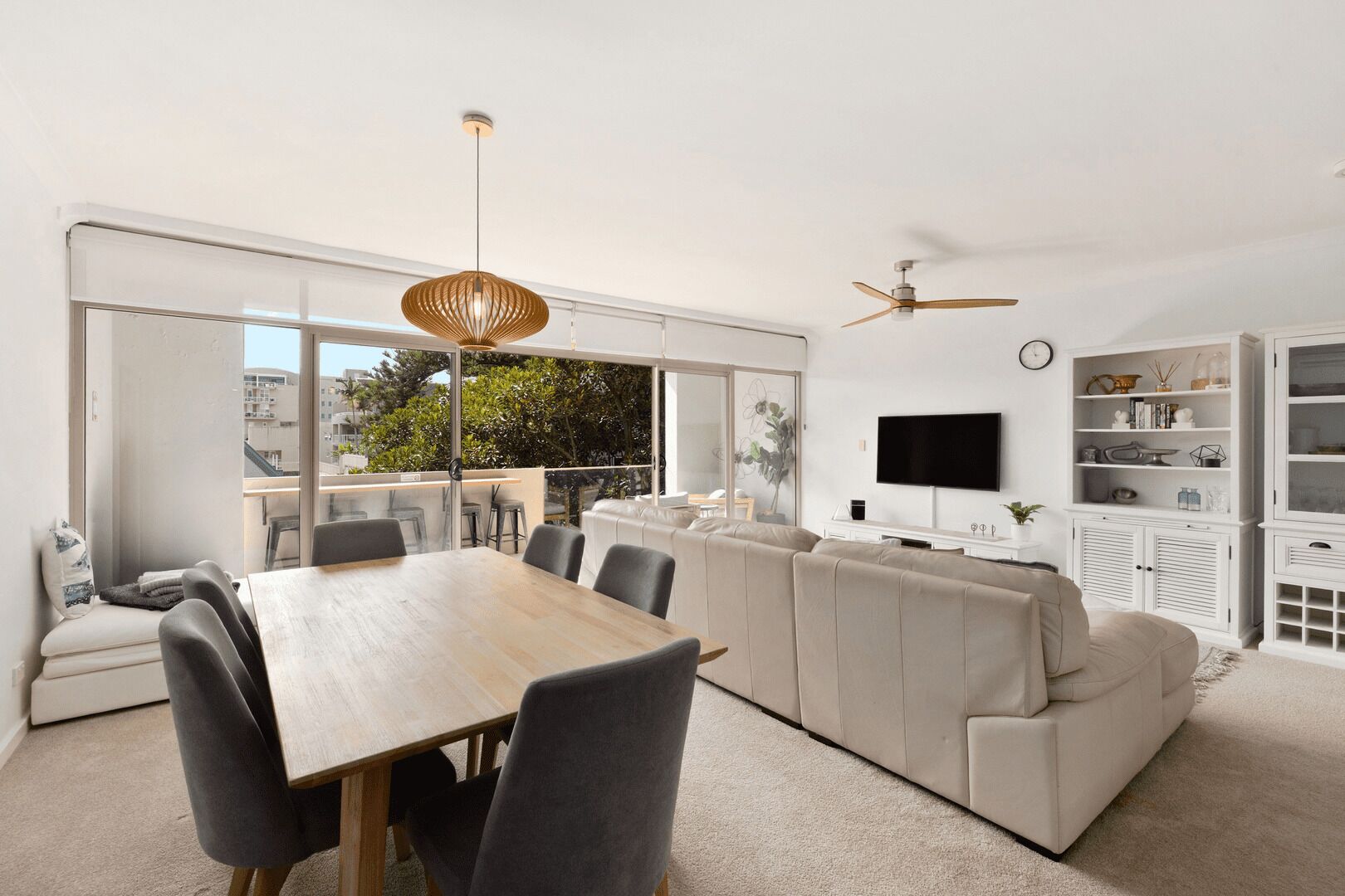 Una sala de estar moderna con comedor, ventanas grandes, ventilador de techo y televisor en la pared.