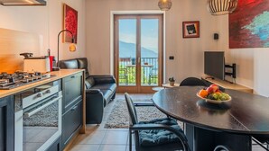A modern kitchen with a gas stove, a dining area with a round table, and a balcony with a view of the mountains. - Lovely apartment for 3 people with WIFI, TV, terrace and panoramic view (Sorico)
