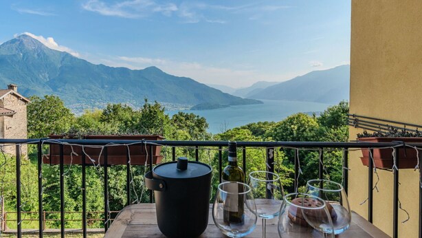 A balcony with a view of mountains and a lake, a wine bottle, and several glasses on a table. - Lovely apartment for 3 people with WIFI, TV, terrace and panoramic view (Sorico)